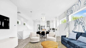 A modern living room with a sofa, chairs, a coffee table, and a kitchen in the background.