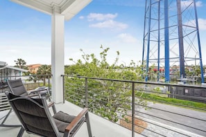 A balcony with outdoor furniture, a view of a blue structure, and greenery.
