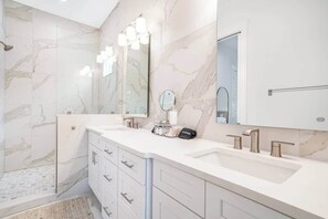A bathroom with marble walls, a double sink vanity, and a shower area.