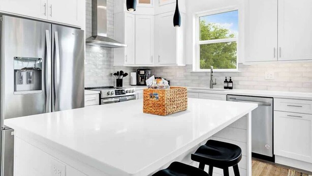 A modern kitchen with white cabinetry, stainless steel appliances, and a large island with stools.