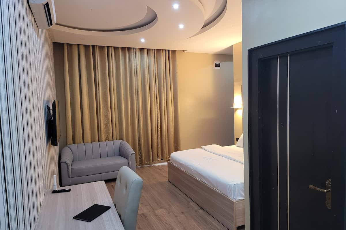 A hotel room with a bed, a sofa, a desk, and a TV.