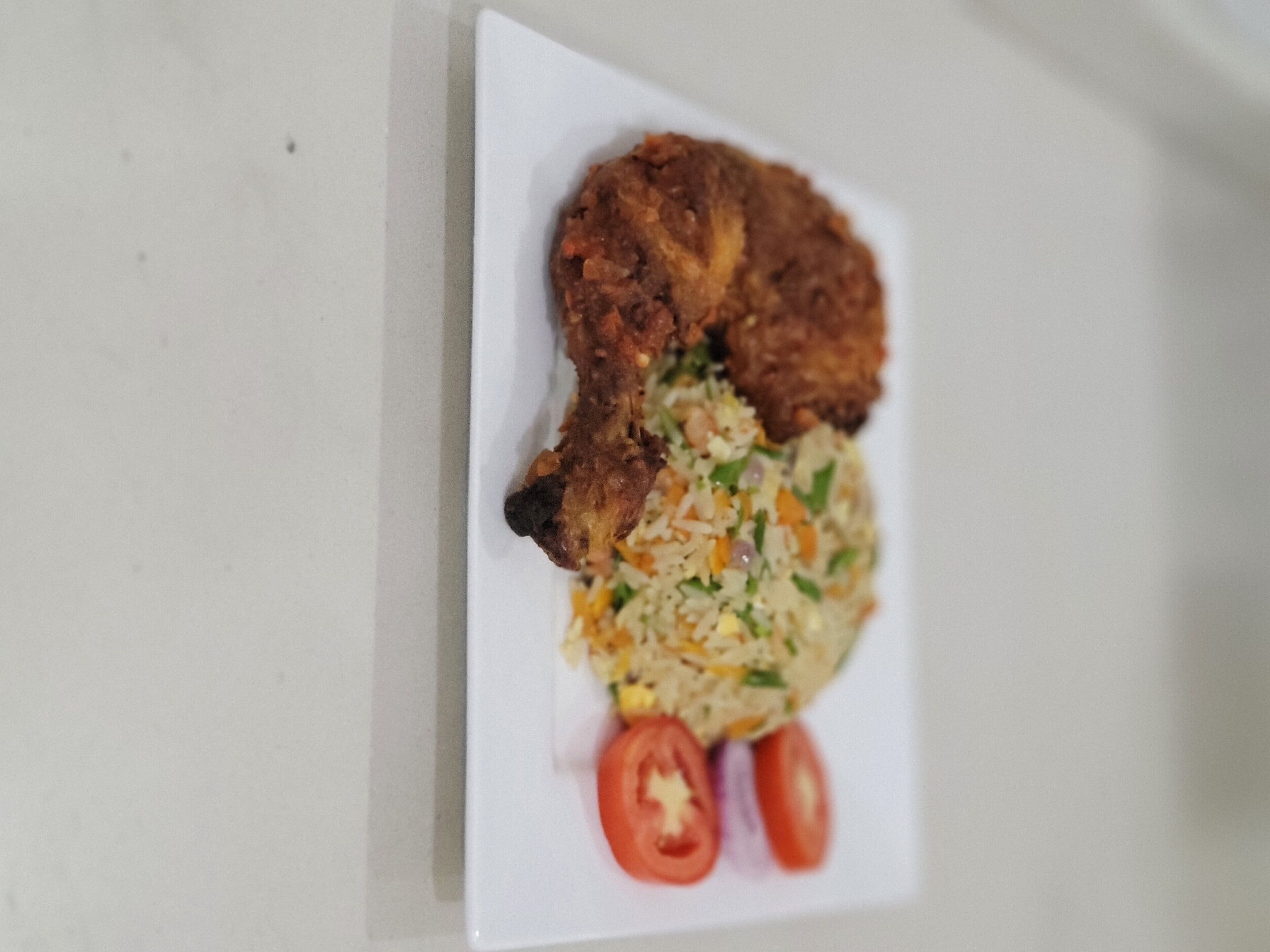 A plate with fried chicken, fried rice, and two tomatoes.