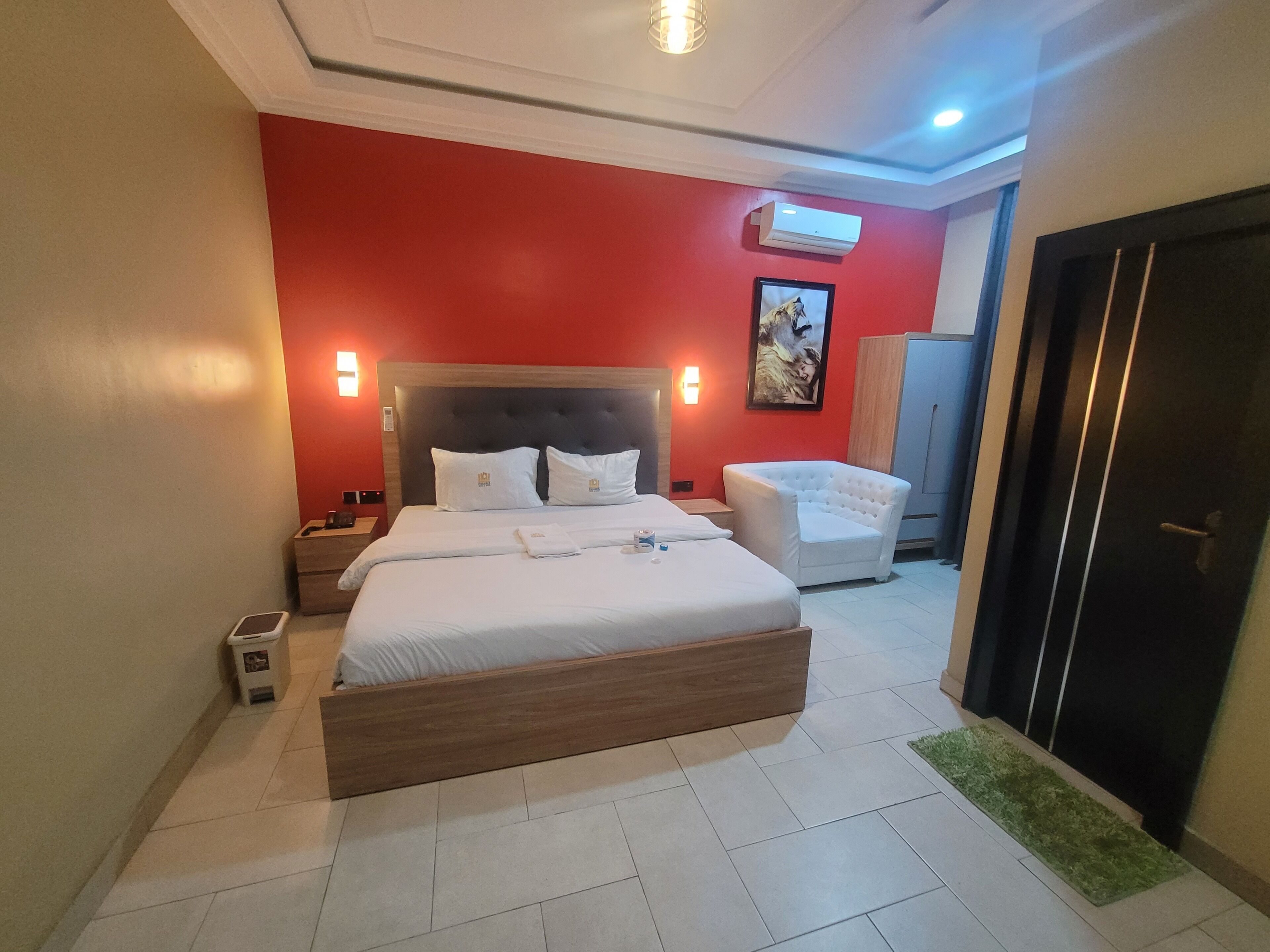 Una habitación de hotel con una cama grande, una mesita de noche, un sillón blanco, un armario y una puerta.