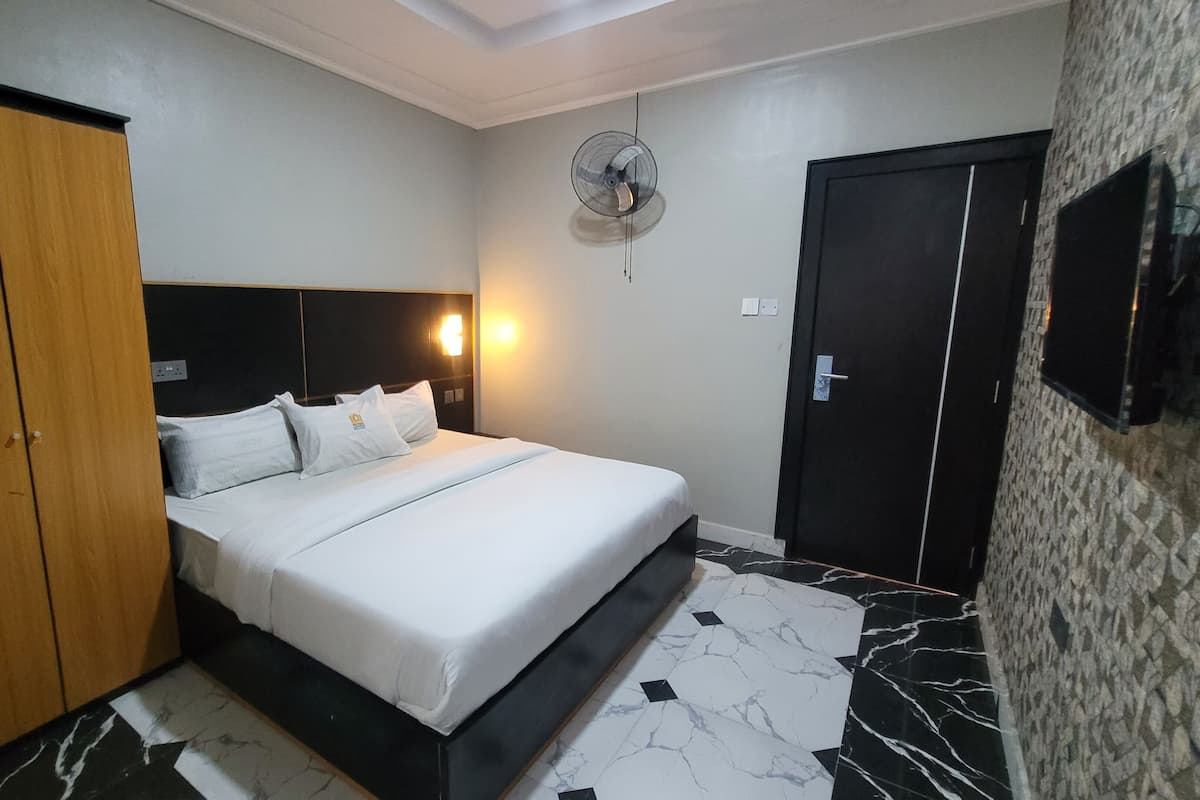 A hotel room with a bed, a wardrobe, a wall-mounted TV, and a ceiling fan.