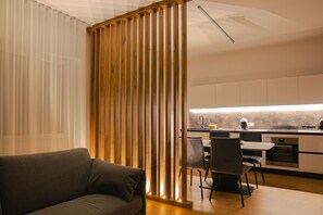 A modern kitchen with a wooden partition, a dining area with chairs, and a sofa in a living room.