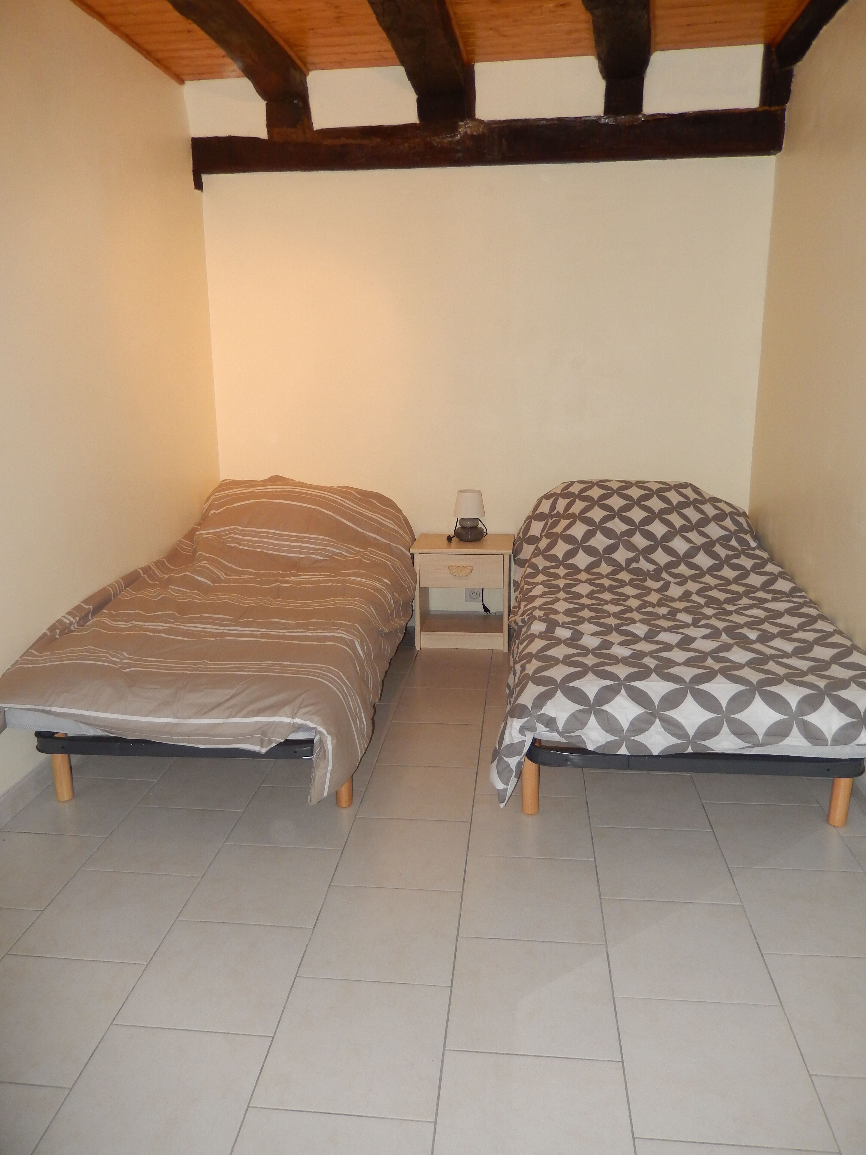Un dormitorio con dos camas individuales, una mesita de noche, una lámpara y techo de madera.