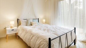 A bedroom with a bed, nightstands, and a window with sheer curtains. - Marathon Luxury Suites - Schinias Beach (Marathon)
