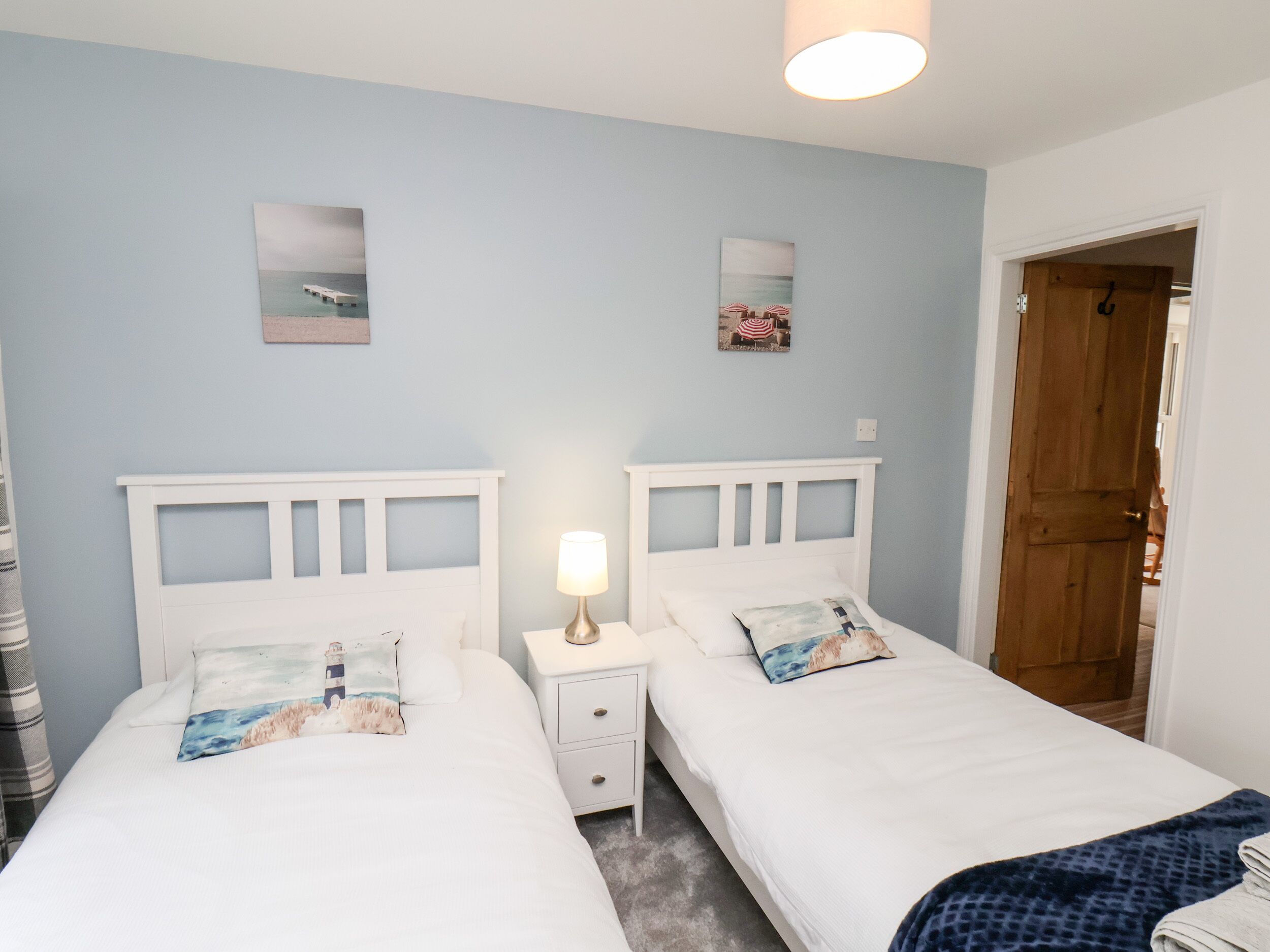 A bedroom with two single beds, a nightstand with a lamp, and a wooden door.