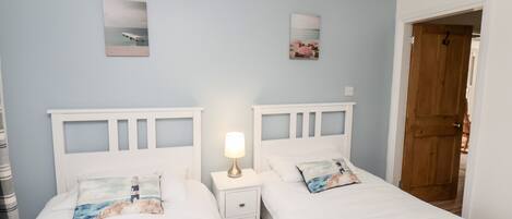 A bedroom with two single beds, a nightstand with a lamp, and a wooden door.