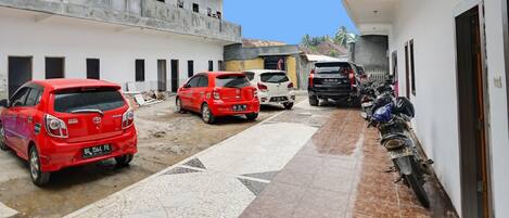 A narrow alley with parked cars and motorcycles, a partially constructed building, and a tiled walkway.