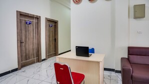 Un espace d’accueil comprenant un comptoir, un fauteuil rouge, un canapé en cuir marron et deux portes en bois avec des panneaux indicateurs.