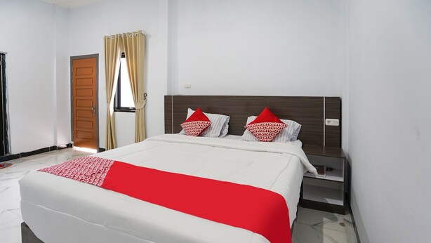 Une chambre d’hôtel avec un grand lit, une table de chevet, une porte en bois et une fenêtre avec des rideaux.