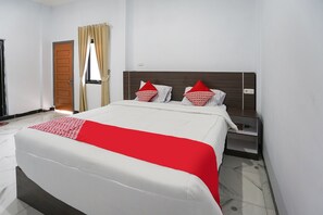 A hotel room with a large bed, a nightstand, a wooden door, and a window with curtains. - OYO 91711 Grand Ansara Mentari Residence (Karya Penggawa)