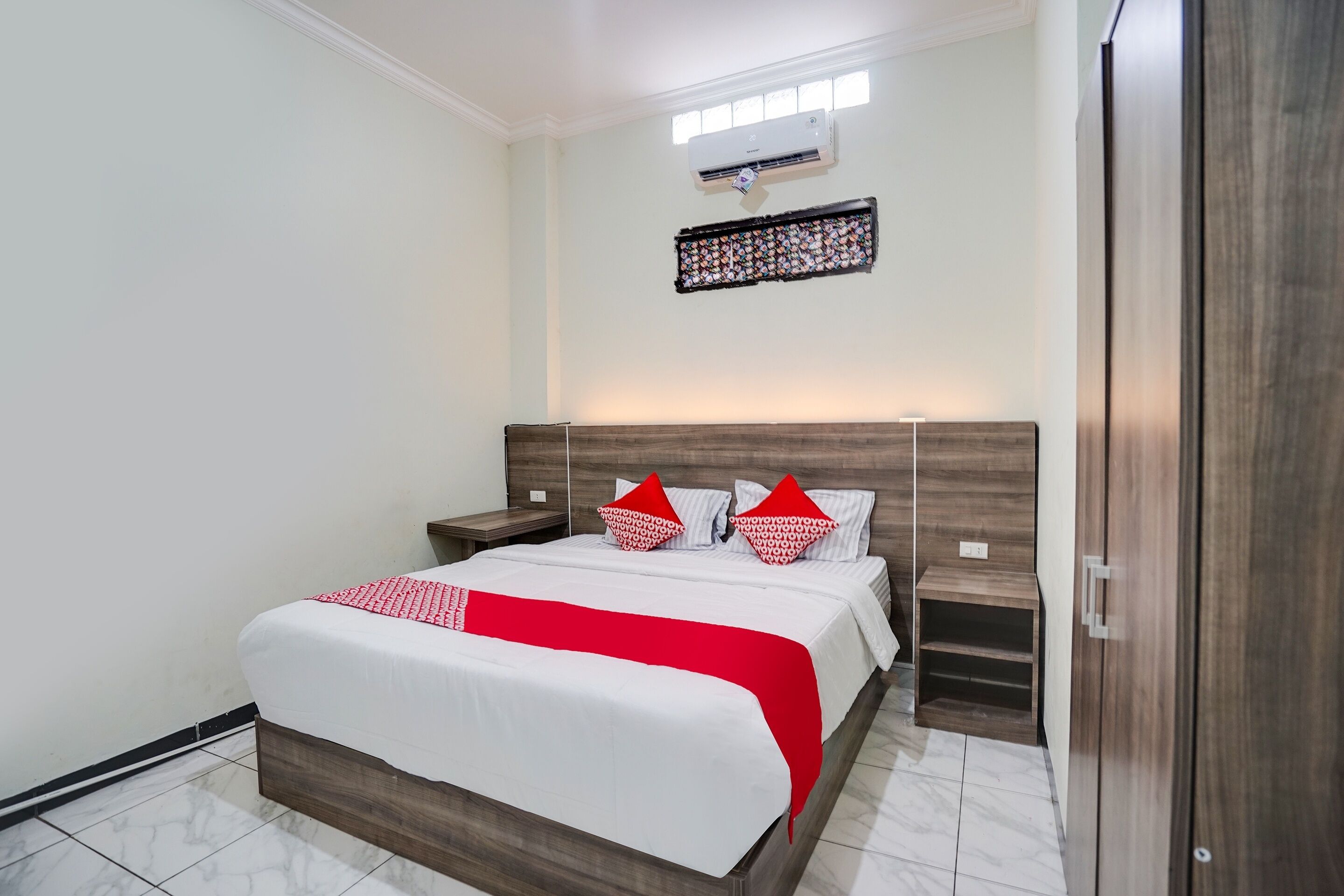A neatly arranged bedroom with a large bed, wooden headboard, bedside tables, and a wall-mounted air conditioner.