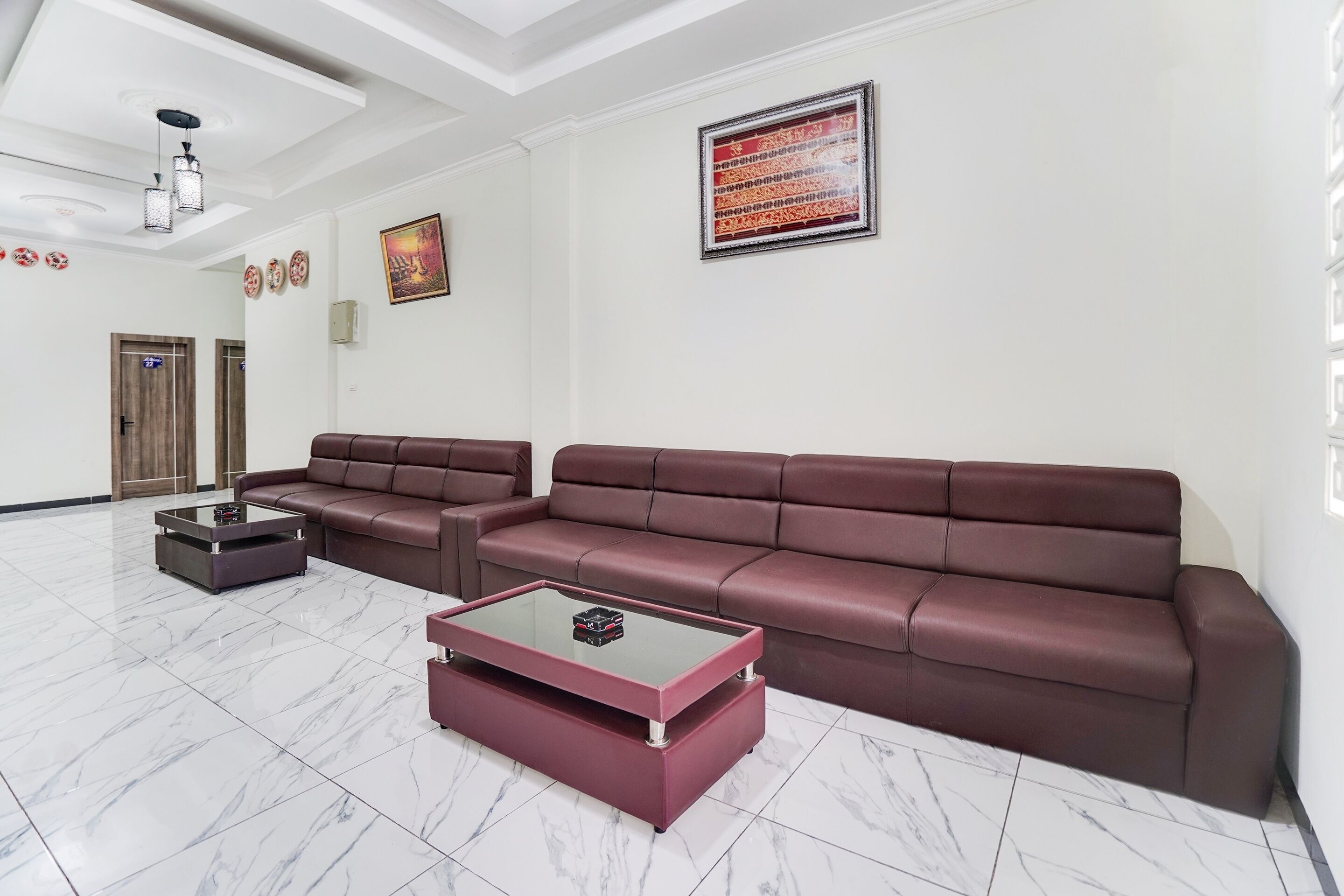 A spacious lobby with a large brown leather sofa, a glass coffee table, and a marble floor.