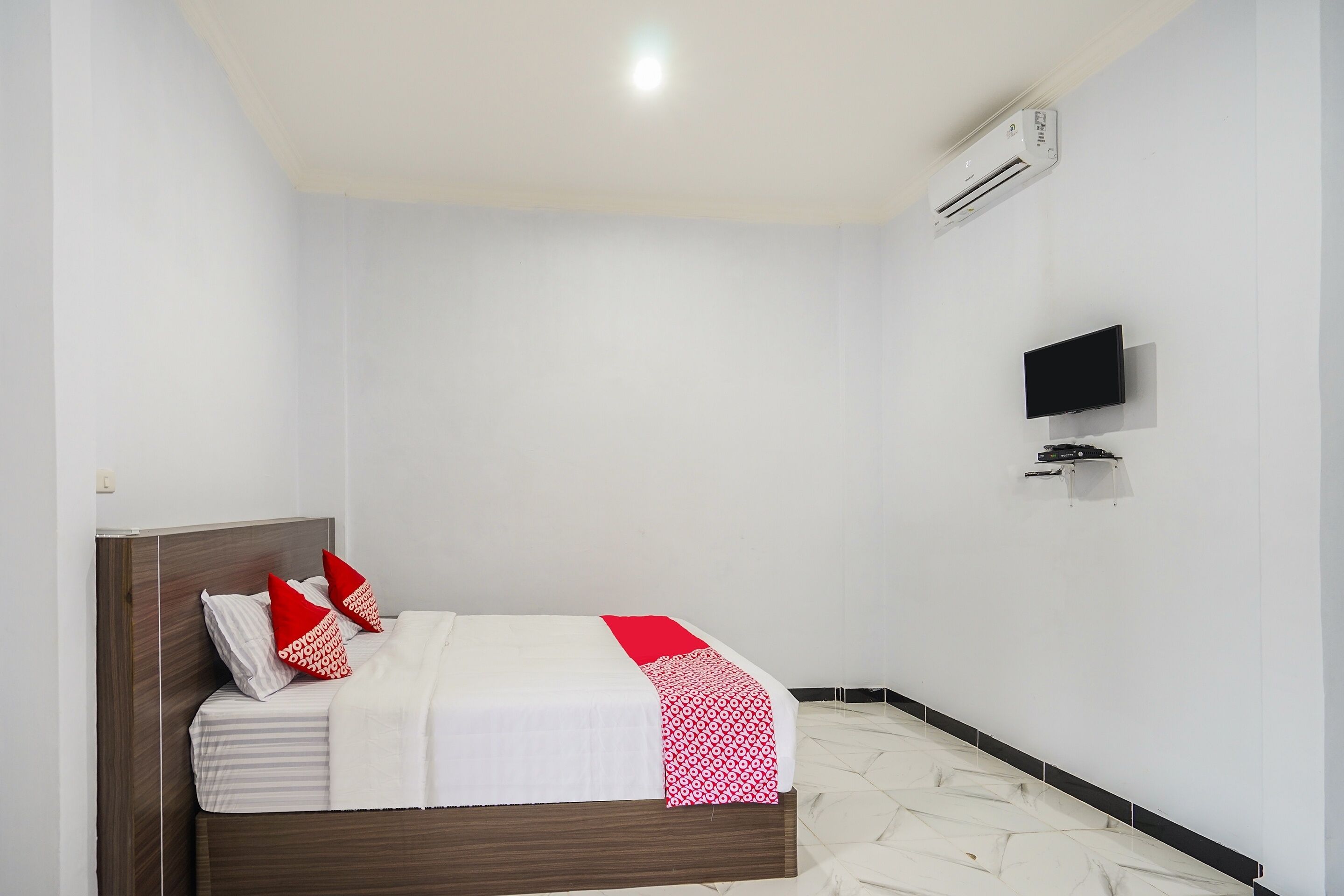 A hotel room with a bed, a flat-screen TV mounted on the wall, and an air conditioning unit.