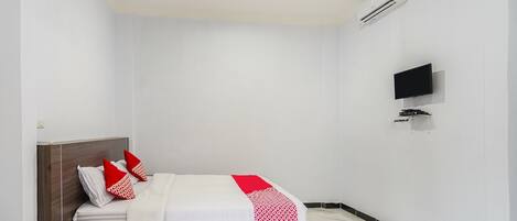 A hotel room with a bed, a flat-screen TV mounted on the wall, and an air conditioning unit.
