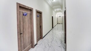 Un couloir avec des portes en bois portant les numéros des chambres, des murs blancs et un sol en marbre.