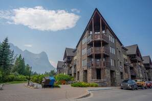 A multi-story hotel with stone and wood exterior, balconies, and a mountain backdrop.