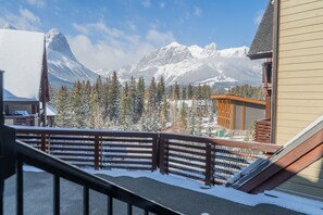 A mountain cabin with a wooden deck and a view of snow-covered mountains.