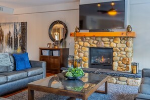 Una sala de estar con chimenea de piedra, un sofá, una mesa de centro y un televisor de pantalla plana montado en la pared.