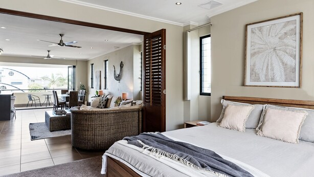A spacious bedroom with a large bed, a balcony with outdoor seating, and a view of the city. - Villa Sangiovese - Unit One - 1-2 Heath Street (Evans Head)