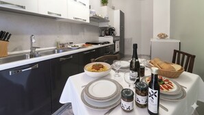 Una cucina moderna con un tavolo da pranzo apparecchiato per due, con una ciotola di pasta, bottiglie di vino e pane.