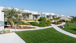 Un hôtel moderne aux murs extérieurs blancs, doté d’un jardin aménagé et offrant une vue sur un ciel dégagé.