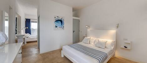 A modern bedroom with a large bed, a bedside table, a mirror, and a wall-mounted light.