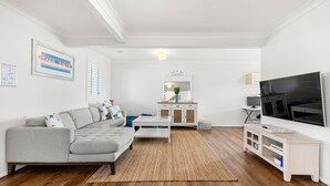 Un salon moderne avec un canapé gris, une table basse, un téléviseur et un coin repas comprenant un buffet blanc et un miroir.