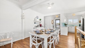 Une cuisine spacieuse avec des meubles blancs, une table à manger en bois pouvant accueillir six personnes et une vue sur l’extérieur.