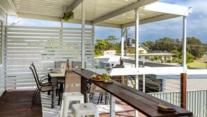 Un espace extérieur abrité, aménagé pour les repas, avec une table en bois, des chaises et une vue sur des immeubles d’habitation.