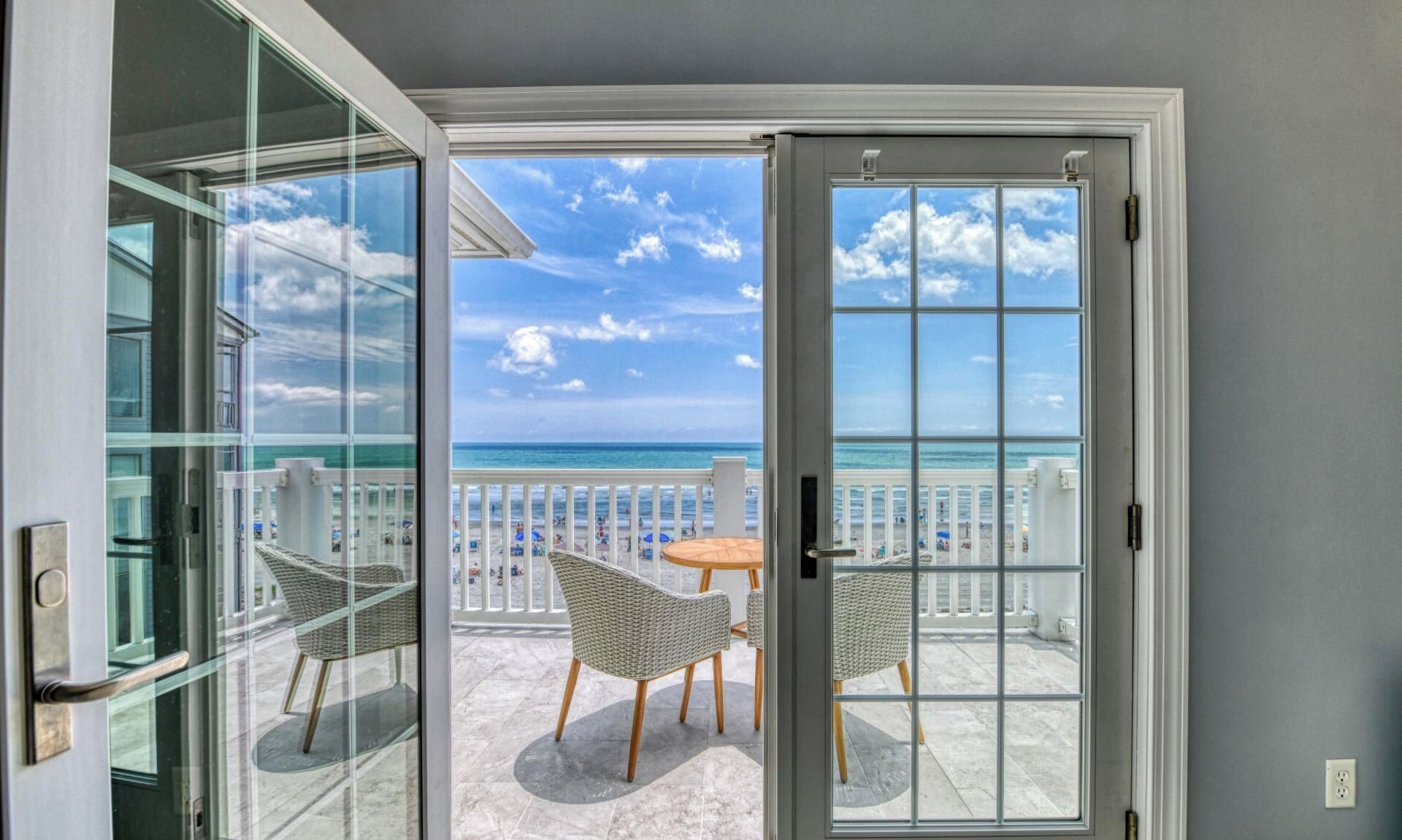 A balcony with a view of the ocean, wicker chairs, and a table.