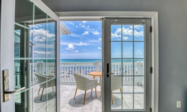 A balcony with a view of the ocean, wicker chairs, and a table.