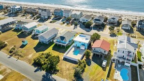 An aerial view of a coastal residential area with houses, a road, and a beach. - Hazel: Oceanview Home with Private Pool (Oak Island)
