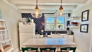 A kitchen with a central island, white appliances, a blue backsplash, and hanging pendant lights. - Hazel: Oceanview Home with Private Pool (Oak Island)