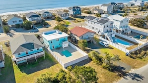 A residential area with houses, a swimming pool, and a beach in the background. - Hazel: Oceanview Home with Private Pool (Oak Island)