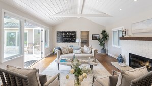Un salón amplio con techo blanco, chimenea y un ventanal que da a un patio.