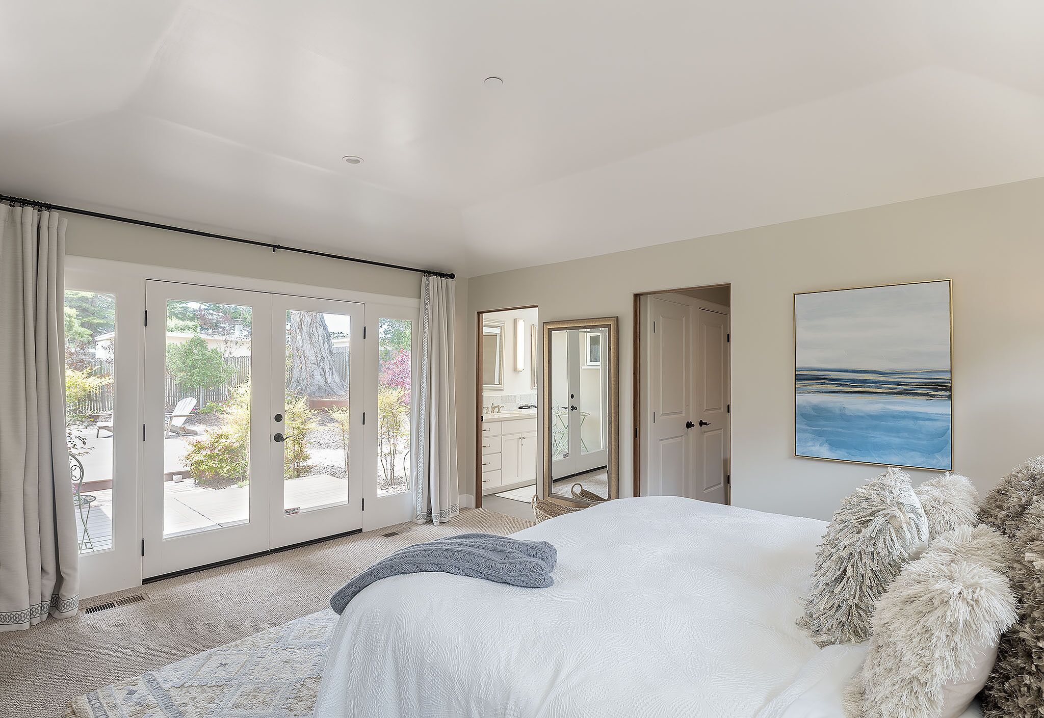 Un dormitorio con una cama grande, vistas a un patio exterior a través de puertas de cristal y un cuadro en la pared.