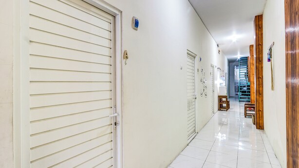 Un pasillo limpio y bien iluminado, con paredes blancas y suelo de baldosas, que conduce a una escalera y una habitación con puerta de madera.