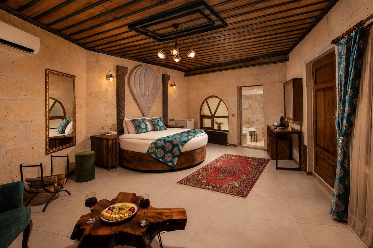 A room with a bed, a dining table with fruit and wine, a mirror, and a wooden ceiling.