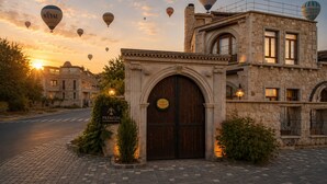 A historic hotel with a prominent arched entrance, a stone facade, and a balcony with a view of the sunset. - Premium Cappadocia Hotel (Nevsehir)