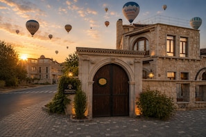 A historic hotel with a prominent arched entrance, a stone facade, and a balcony with a view of the sunset.