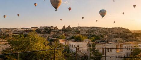 Un paisaje urbano con múltiples globos aerostáticos en el cielo, edificios de arquitectura distintiva y una vista despejada del paisaje circundante.
