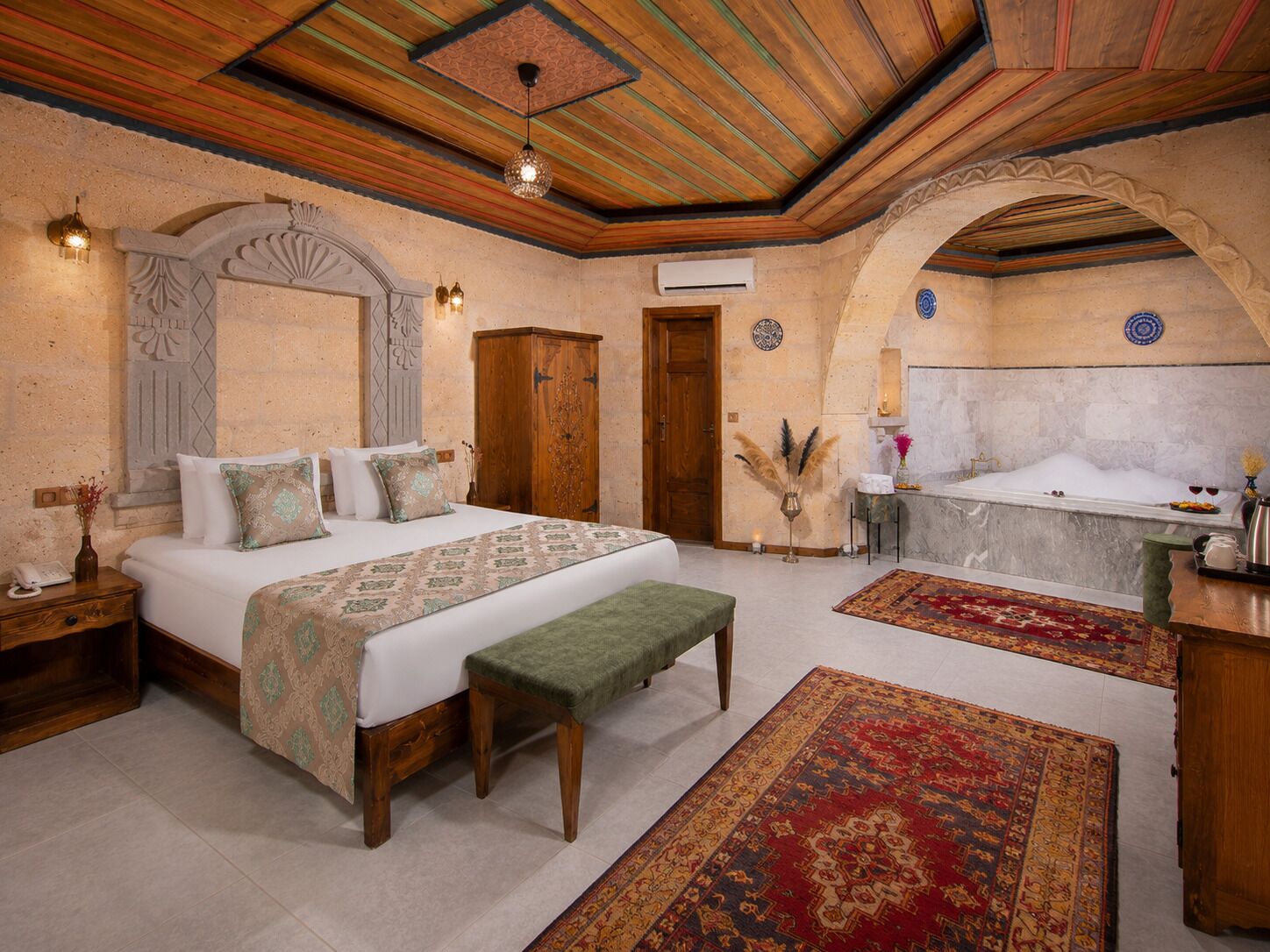 Un dormitorio con una cama grande, un banco, una bañera y una mesita.