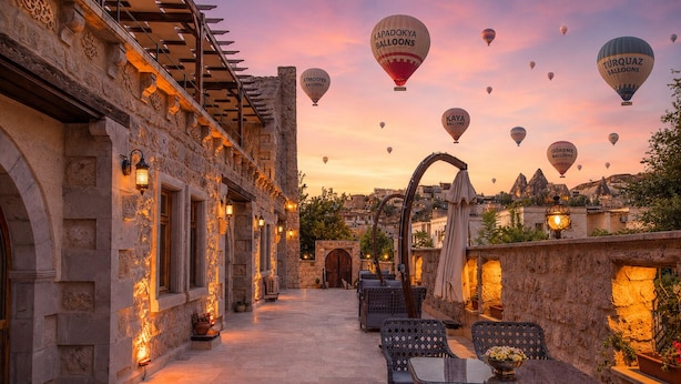 A rooftop terrace with stone walls, outdoor seating, and hot air balloons in the background. - Premium Cappadocia Hotel (Nevsehir)