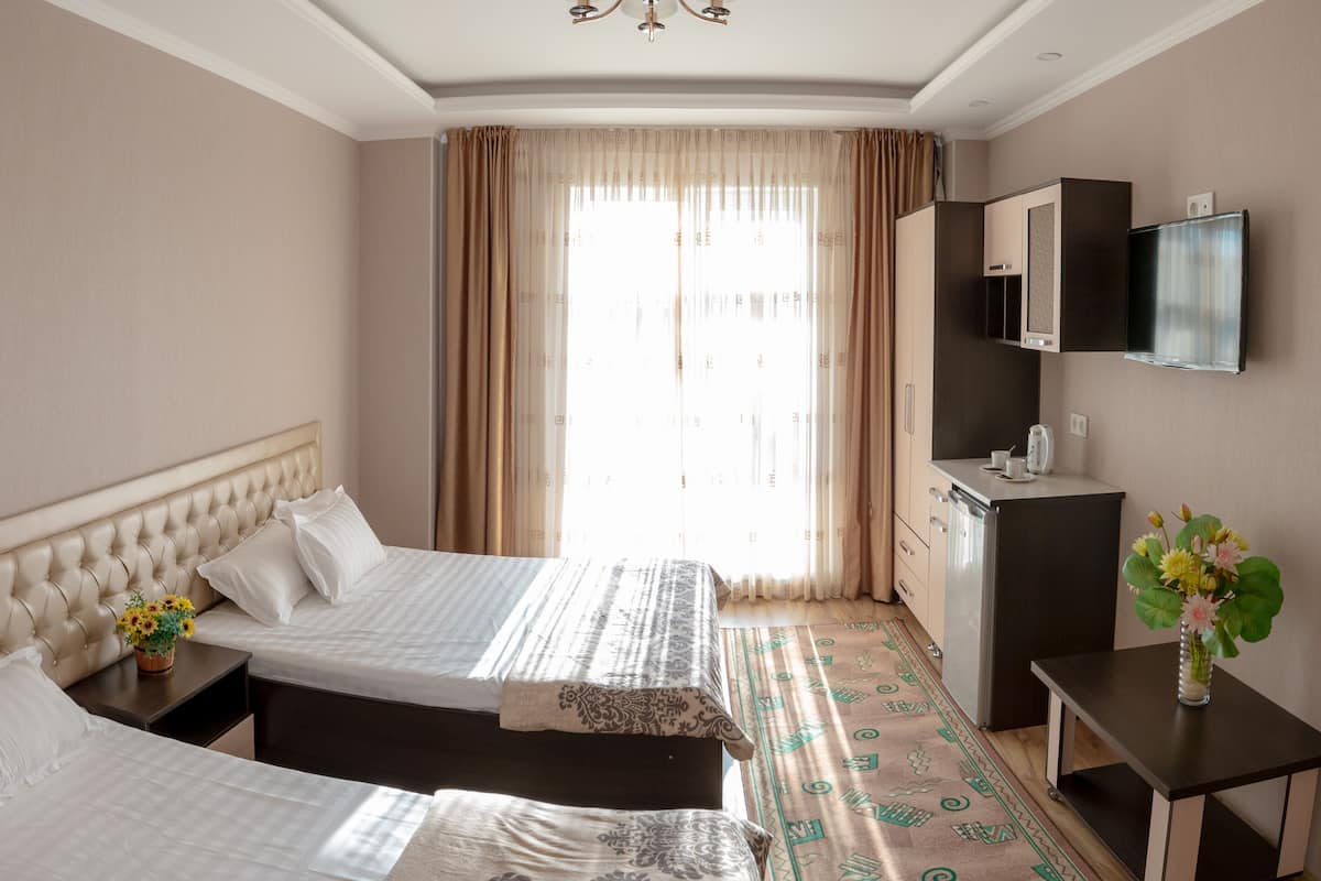 A hotel room with two beds, a TV, a small desk, and a window with curtains.