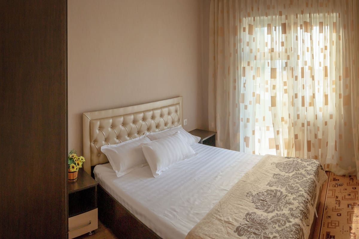 A bedroom with a bed, a nightstand, a lamp, and a window with curtains.