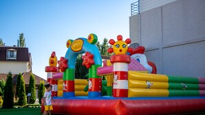 A colorful inflatable play structure with cartoon characters, set on a grassy area with a building in the background. - ololoFamily (Cholpon-Ata)
