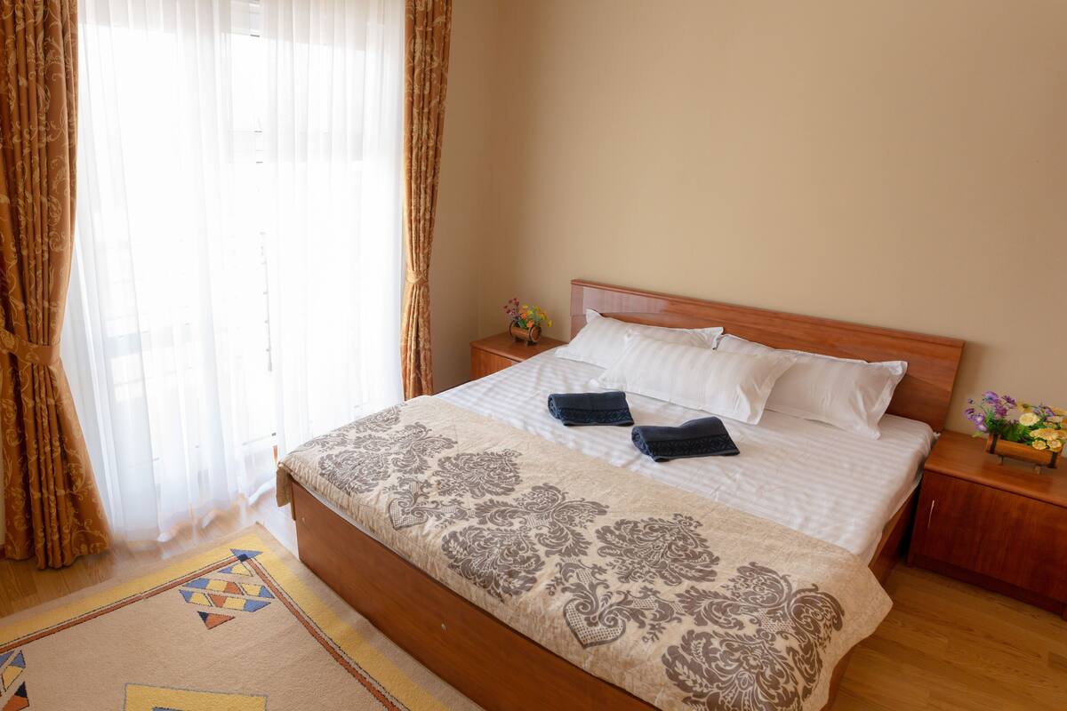 A neatly made bed with a patterned bedspread, a bedside table with a vase of flowers, and a wooden headboard.